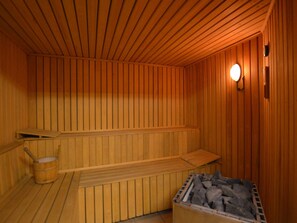 A sauna with wooden walls and benches, a bucket, and a container of rocks. - Holiday Home in Robertville Near Lake & Sauna (Waimes)