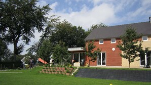 A residential house with a front yard, a patio, and a large tree. - Holiday Home in Robertville Near Lake & Sauna (Waimes)