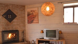 A cozy living room with a fireplace, a television on a wooden stand, and a basket on the floor. - Romantic Cottage in Ardennes (Stoumont)