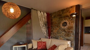 A cozy living room with a sofa, a wooden coffee table, a lamp, and a stone wall. - Romantic Cottage in Ardennes (Stoumont)