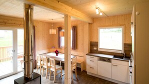 Interno di una baita di legno con zona pranzo, cucina e un'ampia finestra.