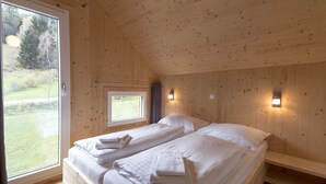Puinen mökkimäinen makuuhuone, jossa on kaksi sänkyä, ikkuna ja pieni kattovalaisin.
