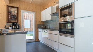 Moderni keittiö, jossa on valkoiset kaapit, ruostumattomasta teräksestä valmistetut kodinkoneet ja puinen katto.