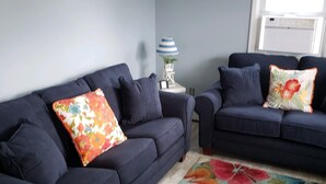 Un salon avec deux canapés bleu foncé, un tapis à motifs floraux aux couleurs vives et une petite table avec une lampe.