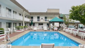 A swimming pool with lounge chairs and a covered area, surrounded by a building with multiple balconies and a parking area. - Ebb Tide Suites (Ocean City)
