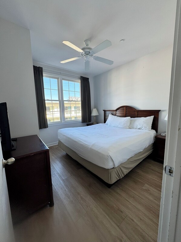 Ein Hotelzimmer mit einem großen Bett, einem Deckenventilator, einem Fernseher und einem Fenster mit Vorhängen.
