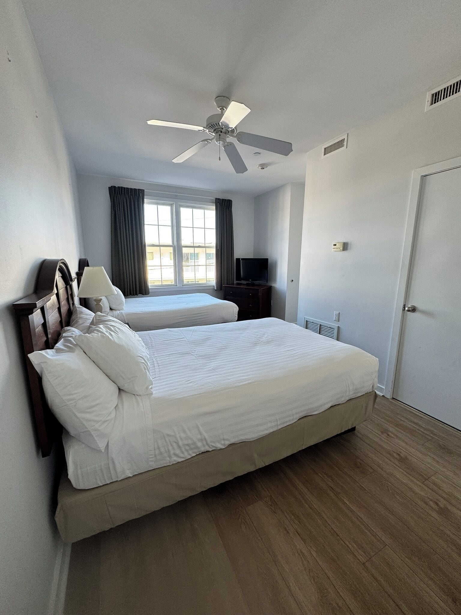 Una camera d'albergo con un letto grande, un ventilatore a soffitto, una TV e una finestra con tende.