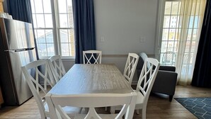 A modern kitchen with a wooden table and white chairs, a refrigerator, and a window with curtains. - Ebb Tide Suites (Ocean City)