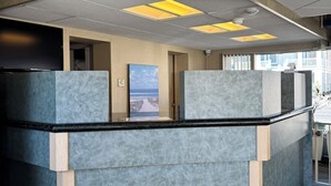 A reception area with a modern design, featuring a counter with a black top and grey panels. There are ceiling lights and a security camera visible. - Ebb Tide Suites (Ocean City)