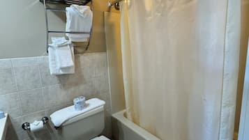 Un baño con inodoro, lavamanos, toallero con toallas y cortina de ducha.