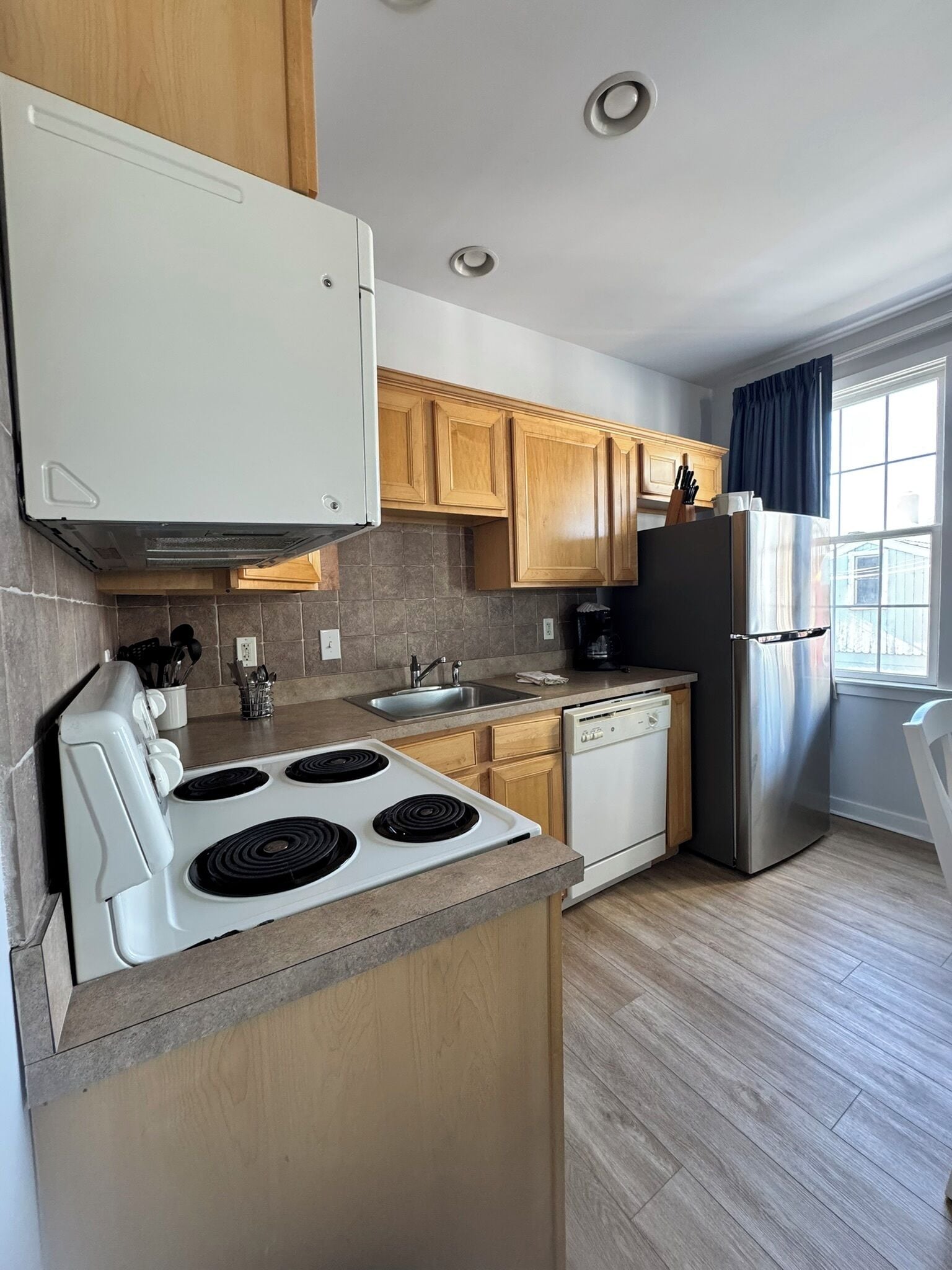 A modern kitchen with a stove, sink, dishwasher, and refrigerator.