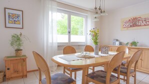 Un coin repas avec une table ronde en bois, six chaises, un vase avec des fleurs et une radio posée sur la table.