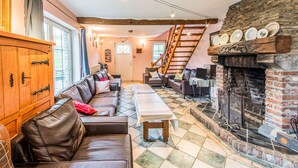A cozy living room with a fireplace, leather sofas, a wooden cabinet, and a staircase.