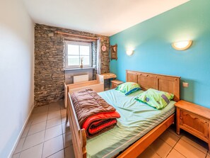 A bedroom with a stone wall, a wooden bed, a window, and a blue wall. - Charming Farmhouse in Brisy (Gouvy)