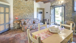 Une pièce rustique avec un mur en pierre, des poutres en bois au plafond, un canapé à motifs, des chaises en osier et une table sur laquelle se trouve un panier.