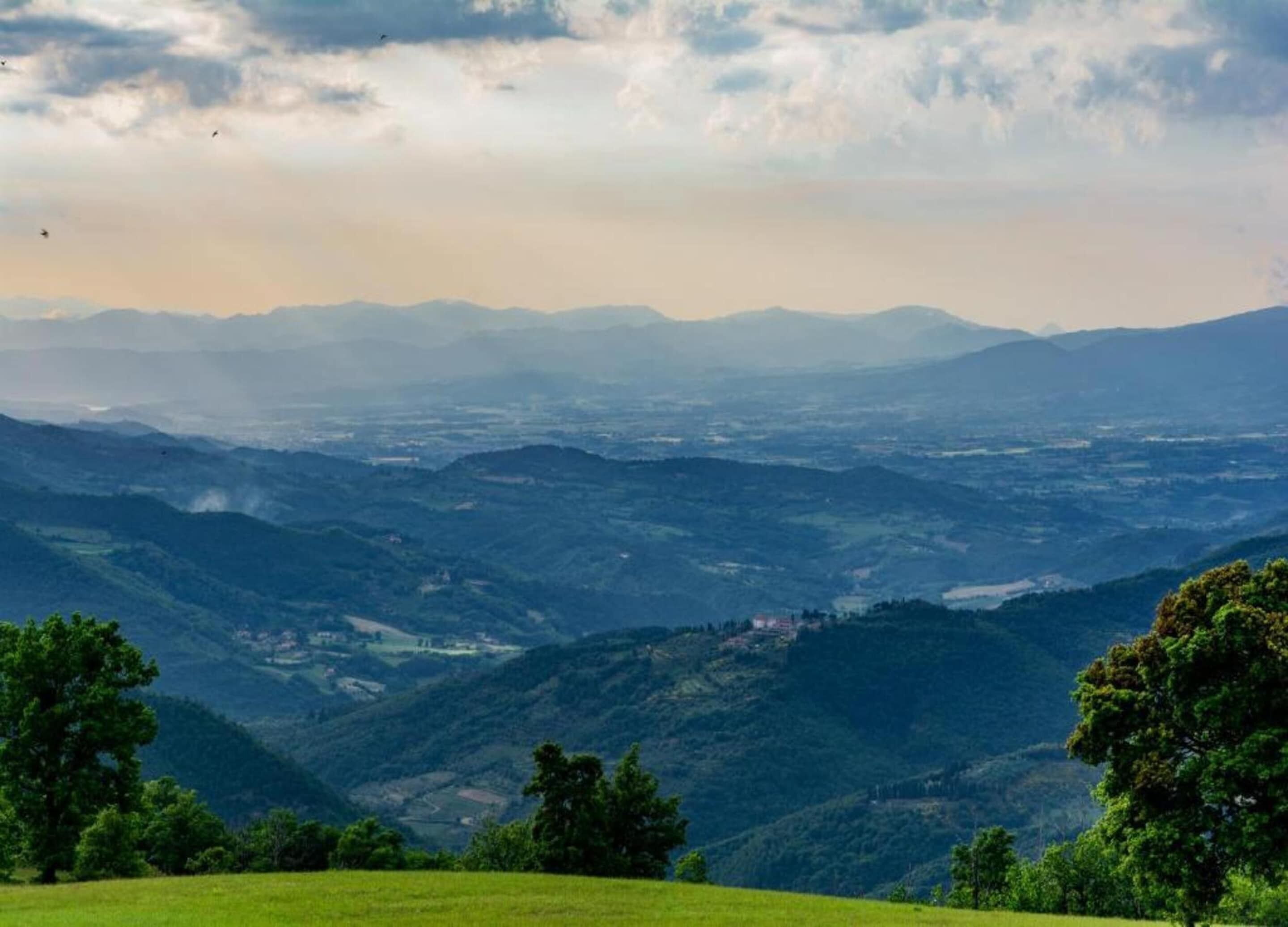 A panoramic view of a mountainous landscape with a valley and scattered buildings.