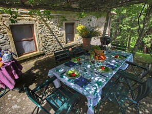 Un espace de restauration en plein air avec un mur en pierre, une table dressée avec des assiettes, des verres et un panier de fruits.