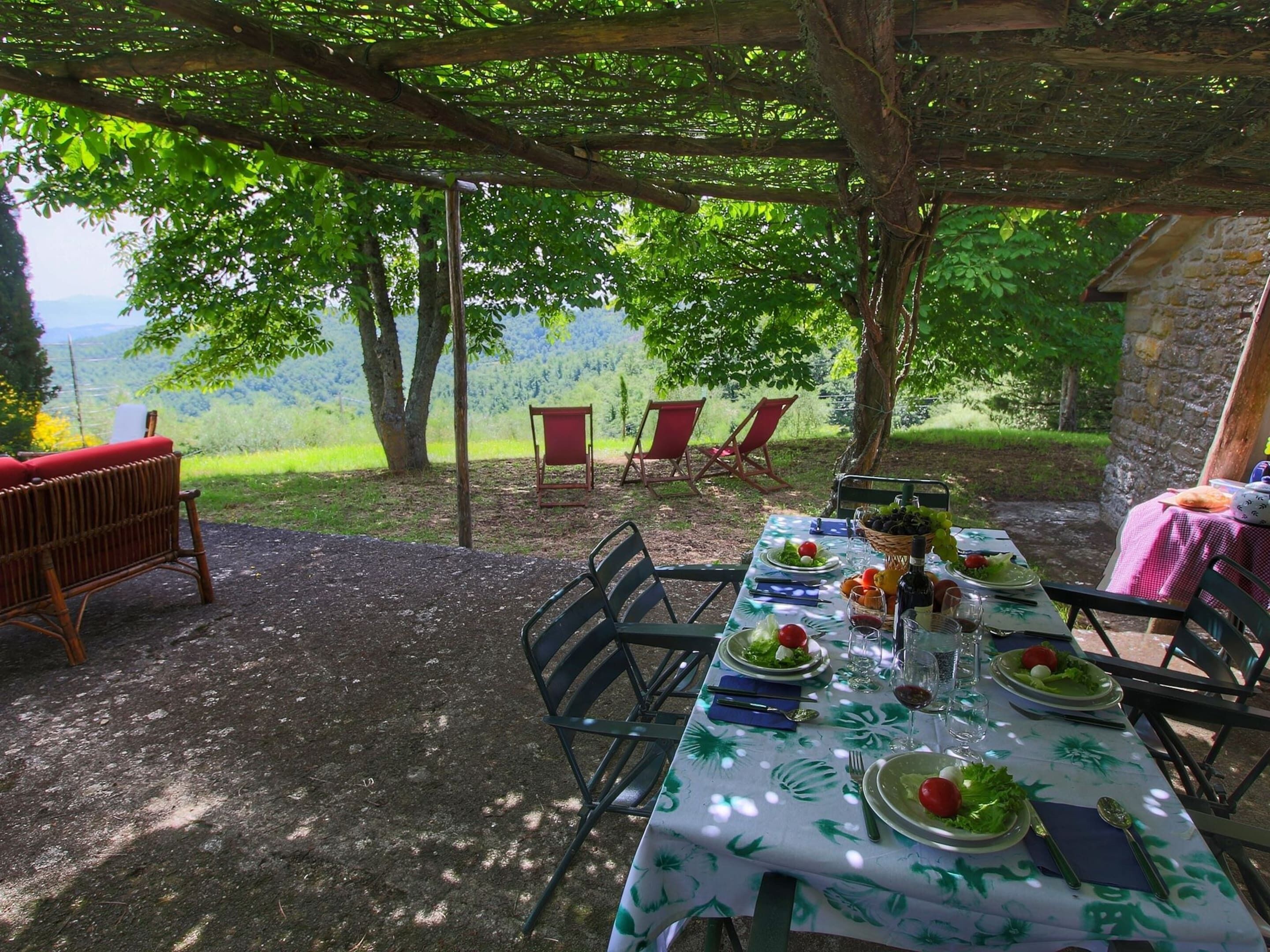 Un'area pranzo all'aperto con un tavolo apparecchiato per quattro persone, circondato da sedie, sotto un pergolato in legno.