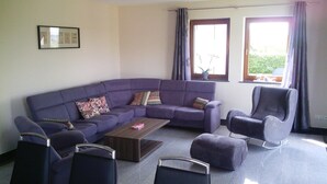 A living room with a purple sofa, two armchairs, a coffee table, and a large window with curtains.