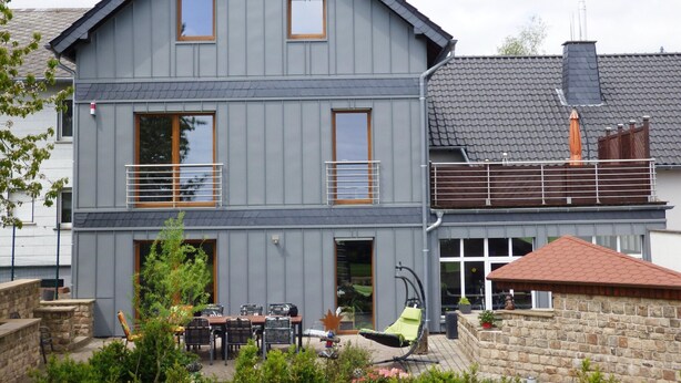A two-story house with a balcony, a patio with outdoor furniture, and a stone wall.
