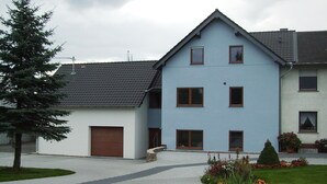 A two-story building with a garage, a small garden with flowers, and a tree.
