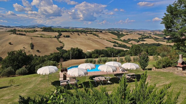 A pool area with umbrellas and lounge chairs, surrounded by rolling hills and a clear sky. - Belvilla by OYO Camino (Arcevia)