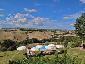 A pool area with umbrellas and lounge chairs, surrounded by rolling hills and a clear sky. - Belvilla by OYO Camino (Arcevia)