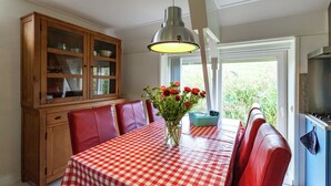 A dining area with a red and white checkered tablecloth, a vase of red flowers, and a wooden cabinet with glass doors. - Peaceful Holiday Home (Anjum)