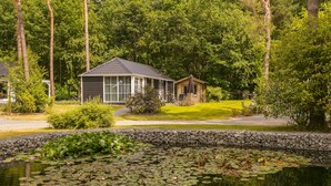 A house with a glass conservatory, surrounded by a pond with lily pads and a stone wall.
