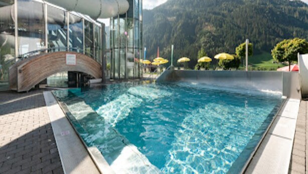 A swimming pool with a glass enclosure, a bridge, and a mountain backdrop.