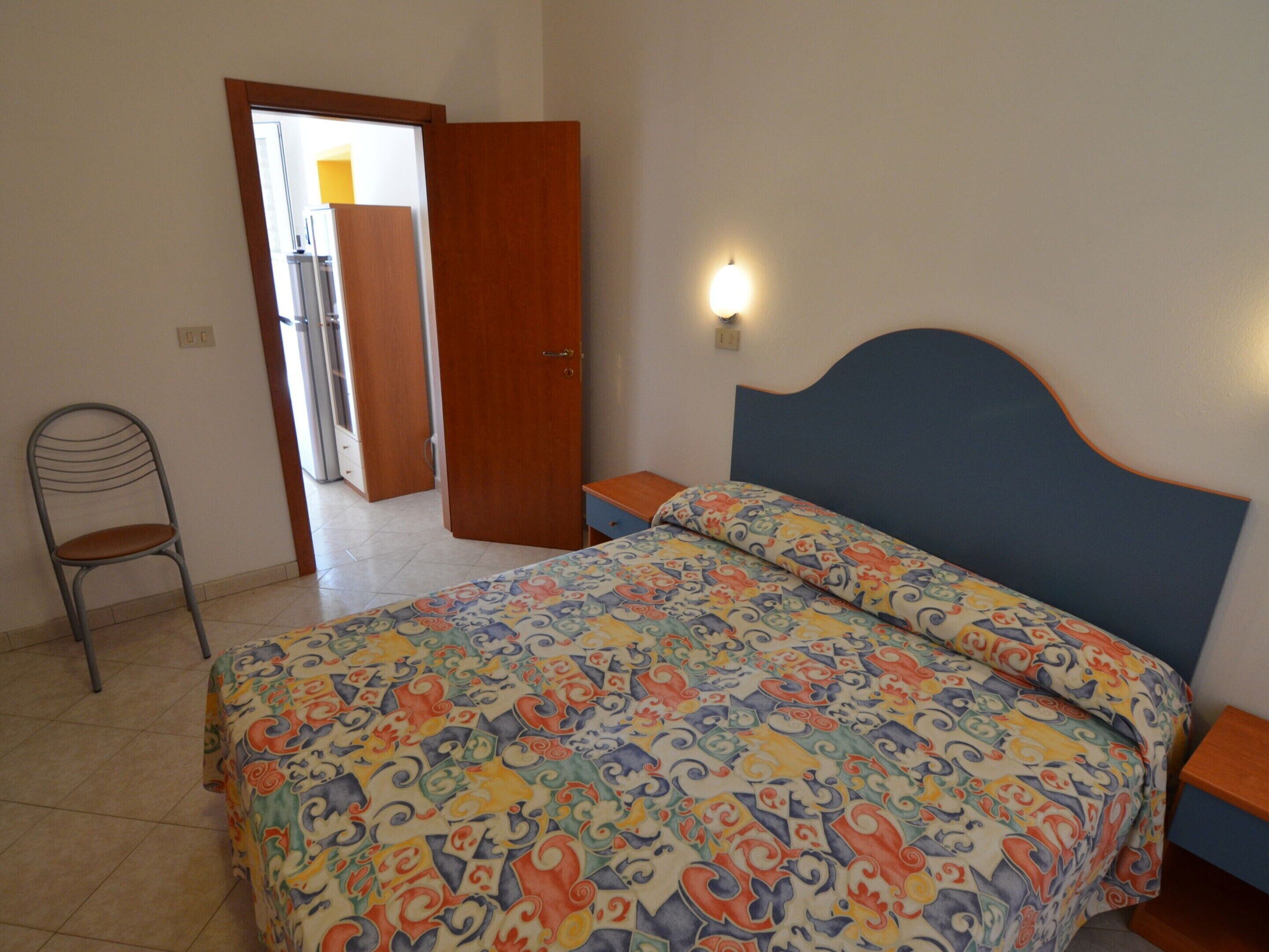 A bedroom with a bed, a chair, and a door leading to another room.