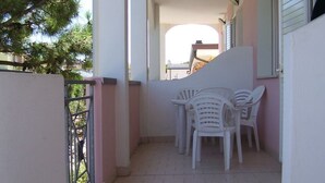 A balcony with white plastic chairs and a table, a metal railing, and a view of a building in the background. - Belvilla by OYO Lido Estensi Trilo Doria (Comacchio)