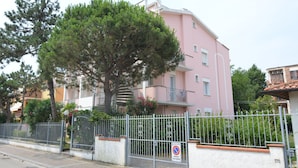 A pink apartment building with a tree in front, a gated entrance, and a no parking sign. - Belvilla by OYO Lido Estensi Trilo Doria (Comacchio)