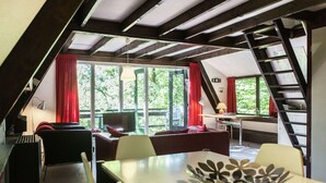 A modern loft-style room with a dining area, a sofa, and a staircase. - Quaint Chalet in Petithan With Roofed Pool (Durbuy)