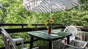 A deck with a table and chairs, a striped umbrella, and a vase with sunflowers. - Quaint Chalet in Petithan With Roofed Pool (Durbuy)