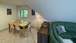 Uma sala de jantar com mesa e cadeiras de madeira, um sofá verde e um abajur.
