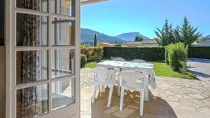 An open patio with a table and chairs, a view of mountains, and a building with a tiled roof.