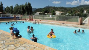 A swimming pool with people, a stone-tiled deck, and a mountainous backdrop.