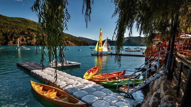 A dock with canoes, a sailboat, and a wooden pier extending into calm water.