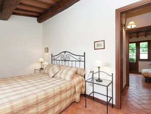 Une chambre à coucher avec un lit, deux tables de chevet avec des lampes, un plafond en bois, un tableau encadré au mur et une porte donnant sur une autre pièce.