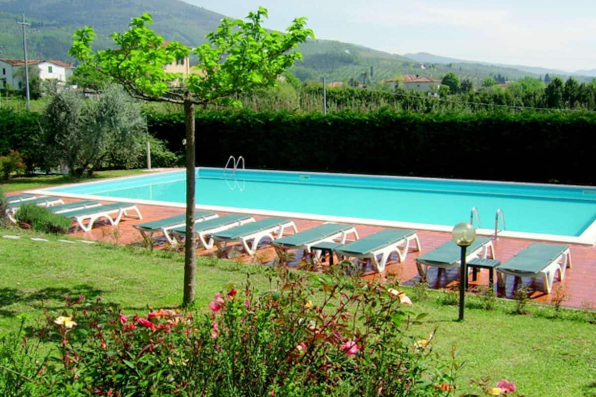 Une piscine avec des chaises longues et un petit espace aménagé en jardin.