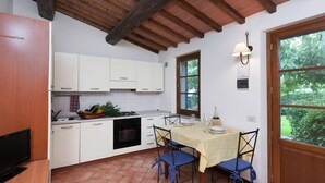 Una cocina con armarios blancos, una mesa de comedor con sillas azules, una ventana y una puerta.