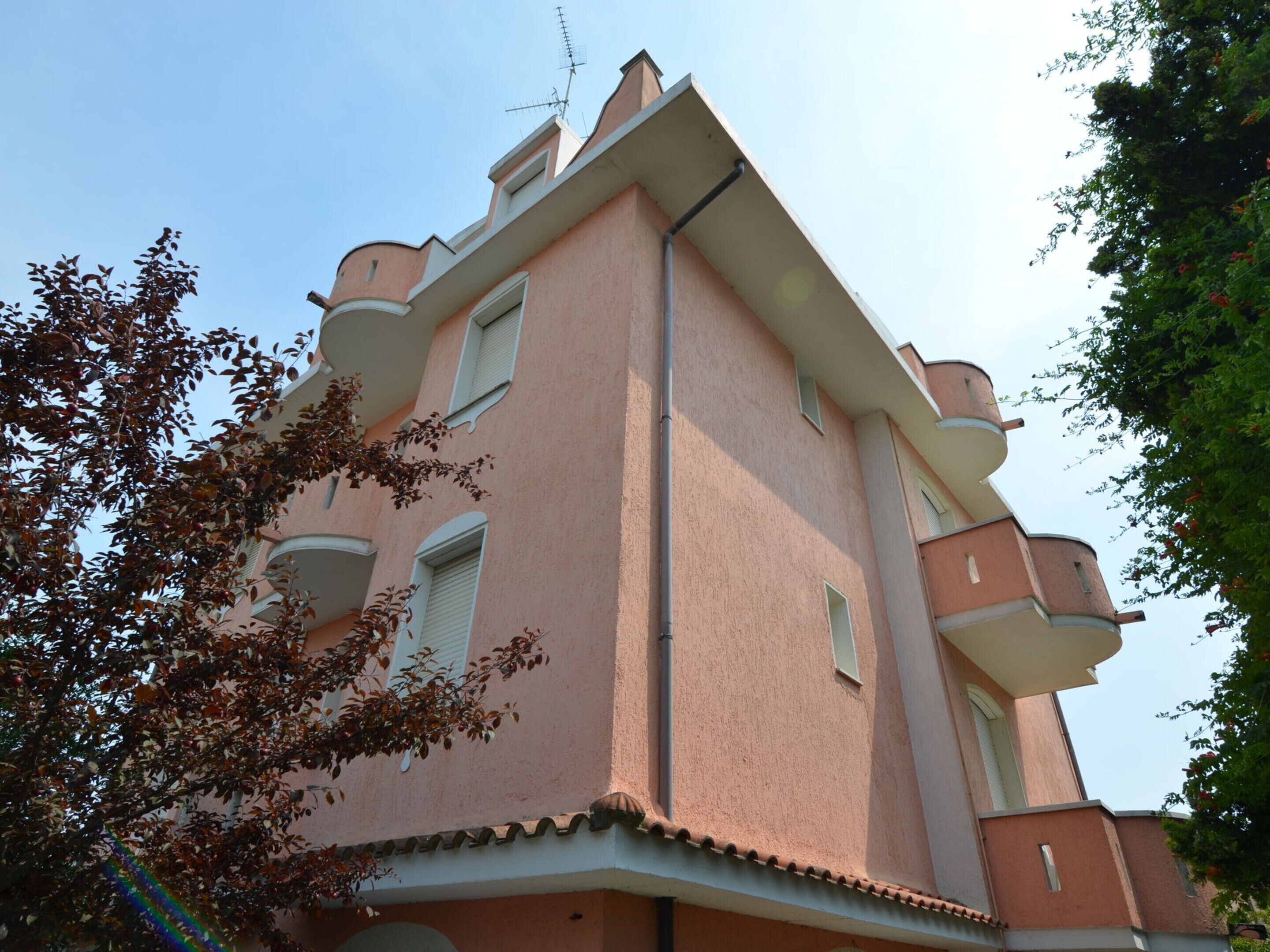 Un immeuble à plusieurs étages, doté d’une façade rose, de balcons et d’une antenne visible.
