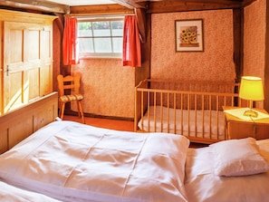 A cozy room with a bed, a crib, a chair, and a window with curtains. - Heritage Holiday Home in Wienhausen near River (Wienhausen)