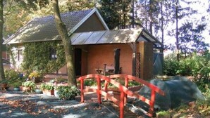 Ein kleines Backsteinhaus mit einer Metallbedeckung, eine rote Brücke und ein Garten mit verschiedenen Pflanzen.