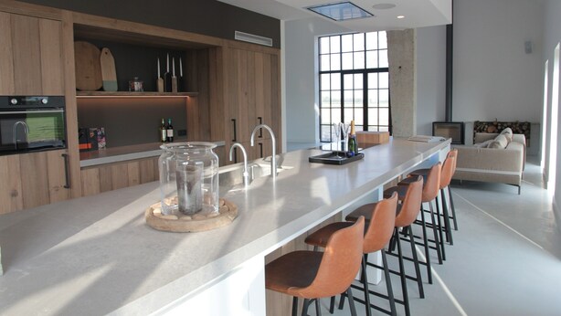 A modern kitchen with a long island, bar stools, and a large window providing natural light. - Villa in Zealand Near Dutch Flanders Coast (Zuidzande)