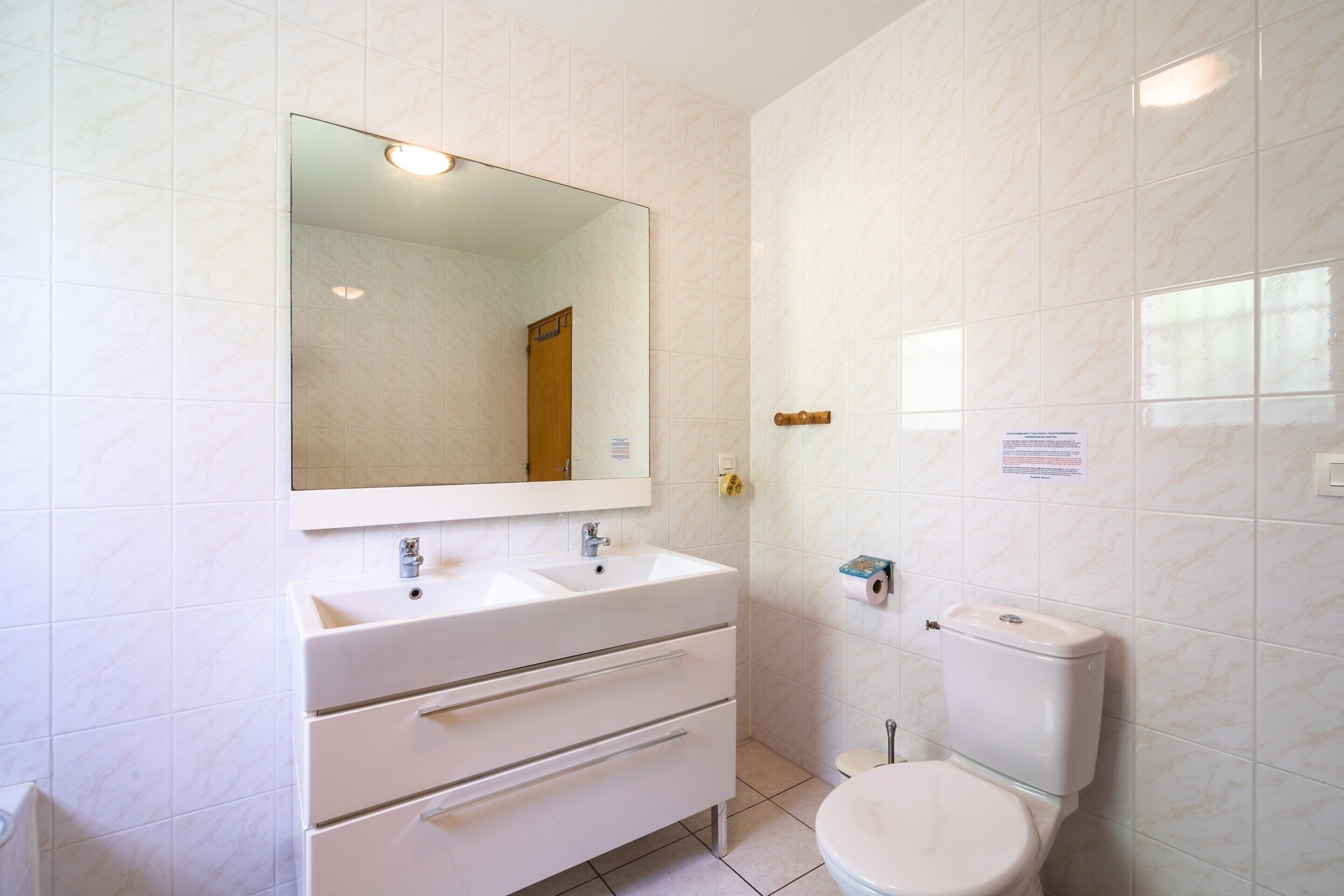 Un baño con lavamanos, espejo y retrete blancos.