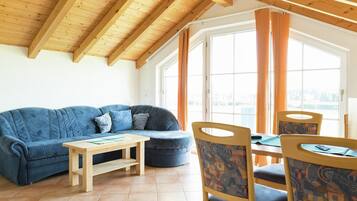 A cozy room with a wooden ceiling, a blue sofa, a small table, and chairs with patterned upholstery.