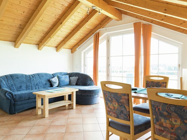 Une pièce chaleureuse avec un plafond en bois, un canapé bleu, une petite table et des chaises recouvertes d’un tissu à motifs.
