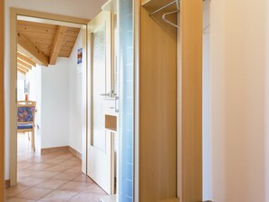 Un couloir avec un plafond en bois, un sol carrelé et une porte dotée d’un panneau en verre dépoli.